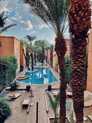 A pool area with palm trees, lounge chairs, and a clear sky. - 3-bedroom riad in amazing Marrakesh with fitness room, AC for family & friends (Marrakesh)