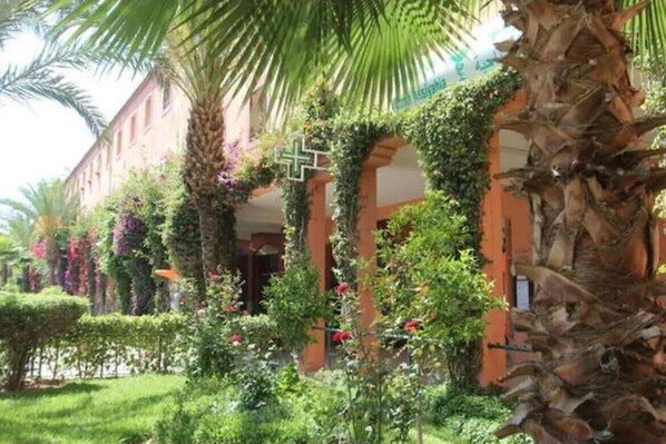 A building with a garden, palm trees, and a cross symbol. - 3-bedroom riad in amazing Marrakesh with fitness room, AC for family & friends (Marrakesh)