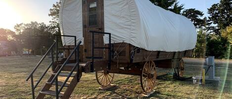 A covered wagon with wooden steps leading up to a door, large wooden wheels, and a white canvas covering.