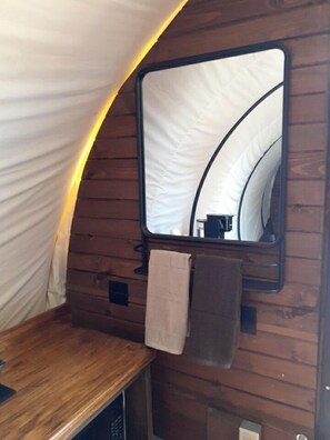 Een tentvormige constructie met een houten interieur, een spiegel en een handdoek aan de muur.