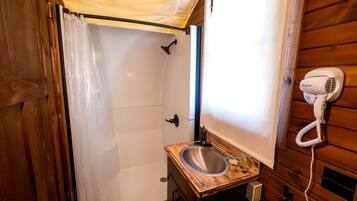 A compact bathroom with a shower, a sink with a wooden countertop, and a hairdryer mounted on the wall.
