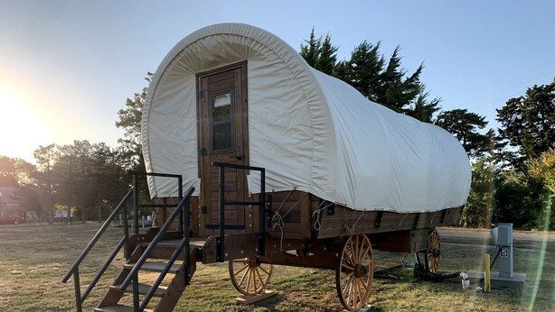A covered wagon with wooden steps leading up to a door, large wooden wheels, and a white canvas covering. - Cozy Covered Wagon for a Unique Glamping Experience in Beaumont, Kansas (Beaumont)