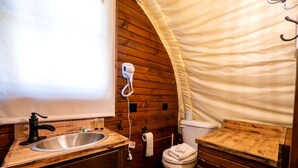 Een kleine badkamer met een houten wastafelmeubel, een wastafel, een toilet en een haardroger bevestigd aan de muur.