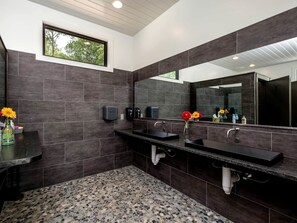 A modern bathroom with dark tiles, a granite countertop, a large mirror, and a window.