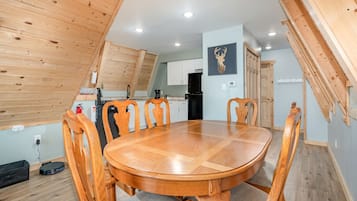 Un comedor con una mesa redonda de madera y sillas, una cocina al fondo y un techo con vigas de madera.