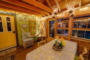 A rustic cabin interior with a hammock, a table with a floral tablecloth, and a chandelier. - Cozy Treehouse with Sauna in Hardwick, VT (Hardwick)