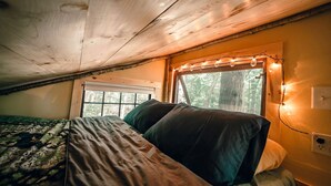 A cozy bedroom with a bed, a window with a view of trees, and string lights on the wall.