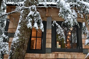 A wooden cabin with a large window and a door, surrounded by snow-covered trees. - Cozy Treehouse with Sauna in Hardwick, VT (Hardwick)