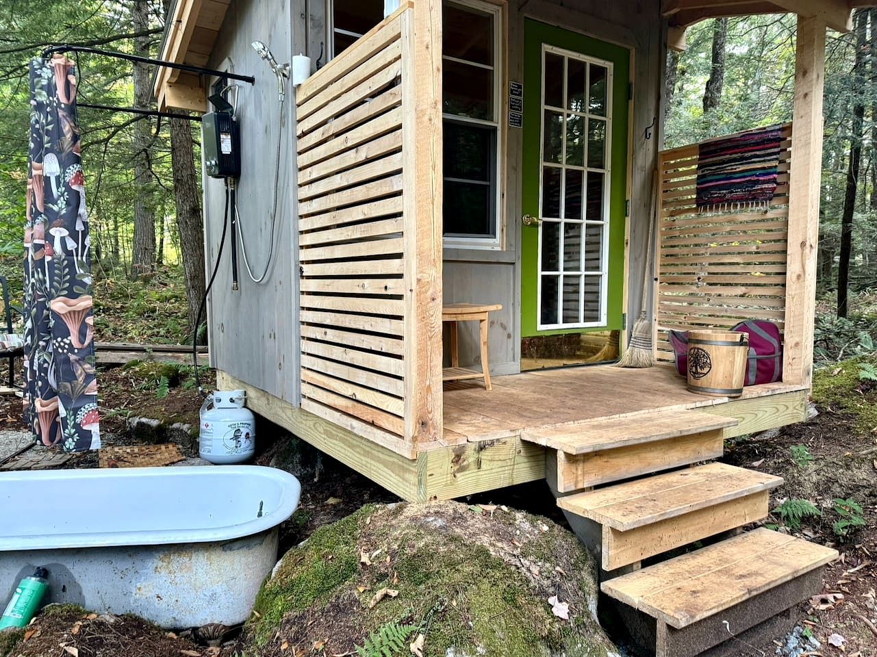 Una cabaña de madera con puerta verde, un porche pequeño y un banco de madera.