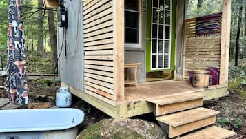 Una cabaña de madera con puerta verde, un porche pequeño y un banco de madera.