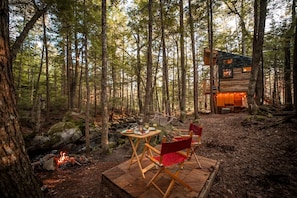 A forest cabin with a dining area featuring a table and chairs, a fire pit, and a wooden deck.