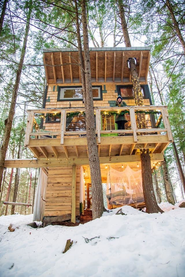 Een boomhut met meerdere niveaus, gebouwd in een bebost gebied met sneeuw op de grond.
