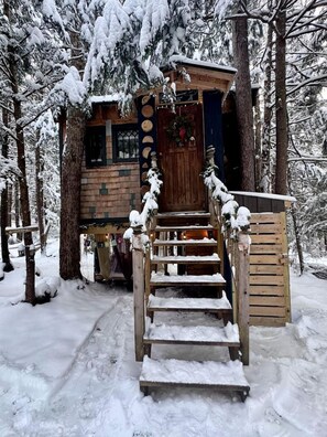 A wooden cabin with a staircase leading to a door, surrounded by snow-covered trees. - Cozy Treehouse with Sauna in Hardwick, VT (Hardwick)