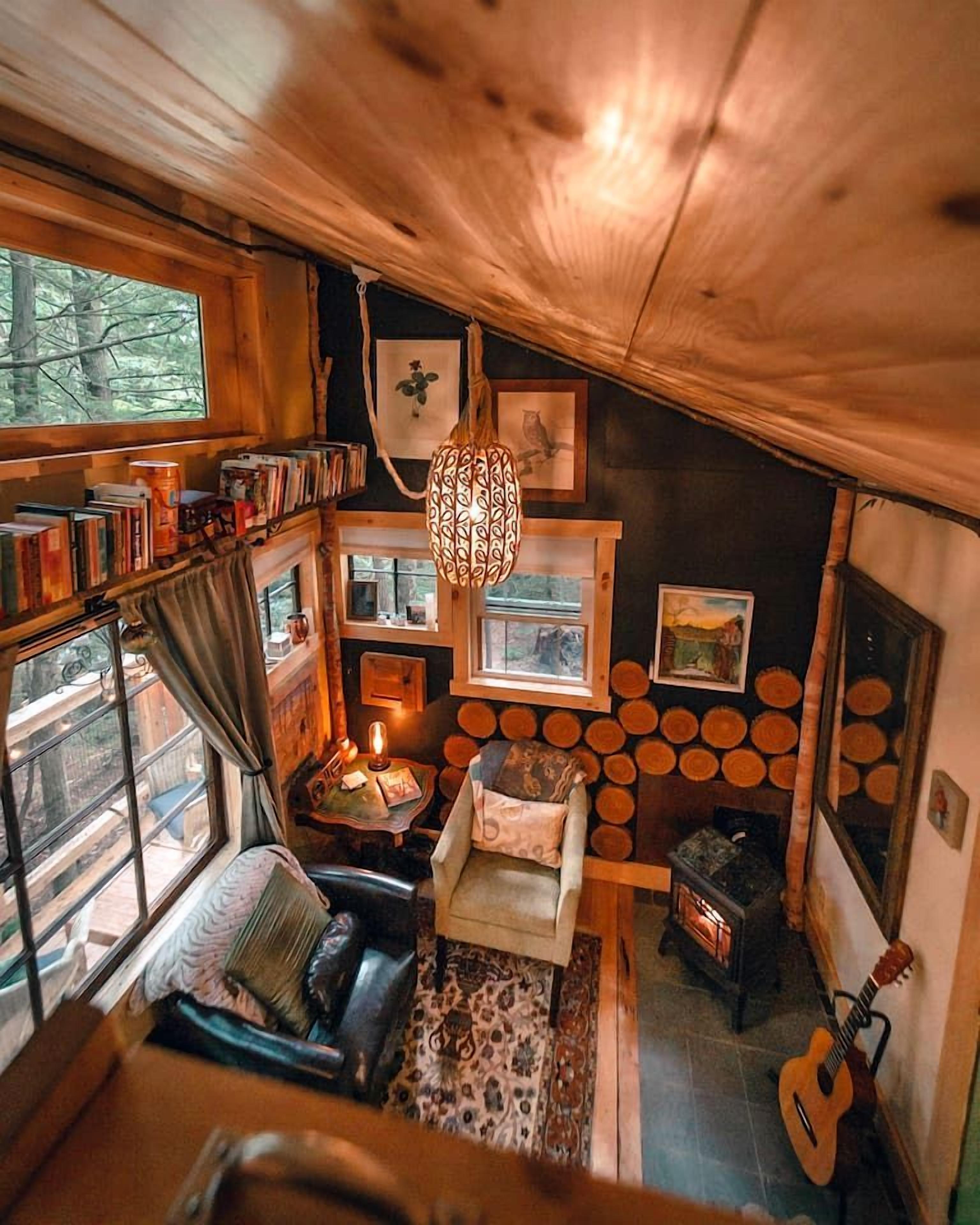 Un acogedor interior de cabaña con chimenea, estanterías, una lámpara colgante y una guitarra.
