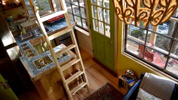 A room with a wooden ladder, a tiled backsplash, a green door, and a view through a window.
