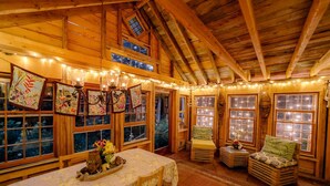 A cozy, rustic interior with wooden beams, a dining area with a table and chairs, and a seating area with a bench.