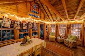 A cozy, rustic interior with wooden beams, a dining area with a table and chairs, and a seating area with a bench.