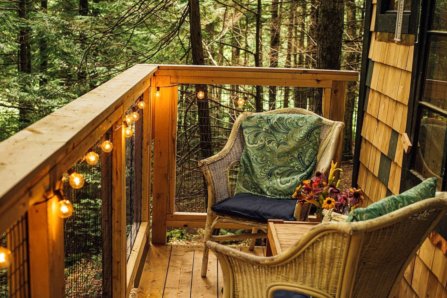 Une terrasse en bois avec une chaise en osier, un coussin et un vase rempli de fleurs.