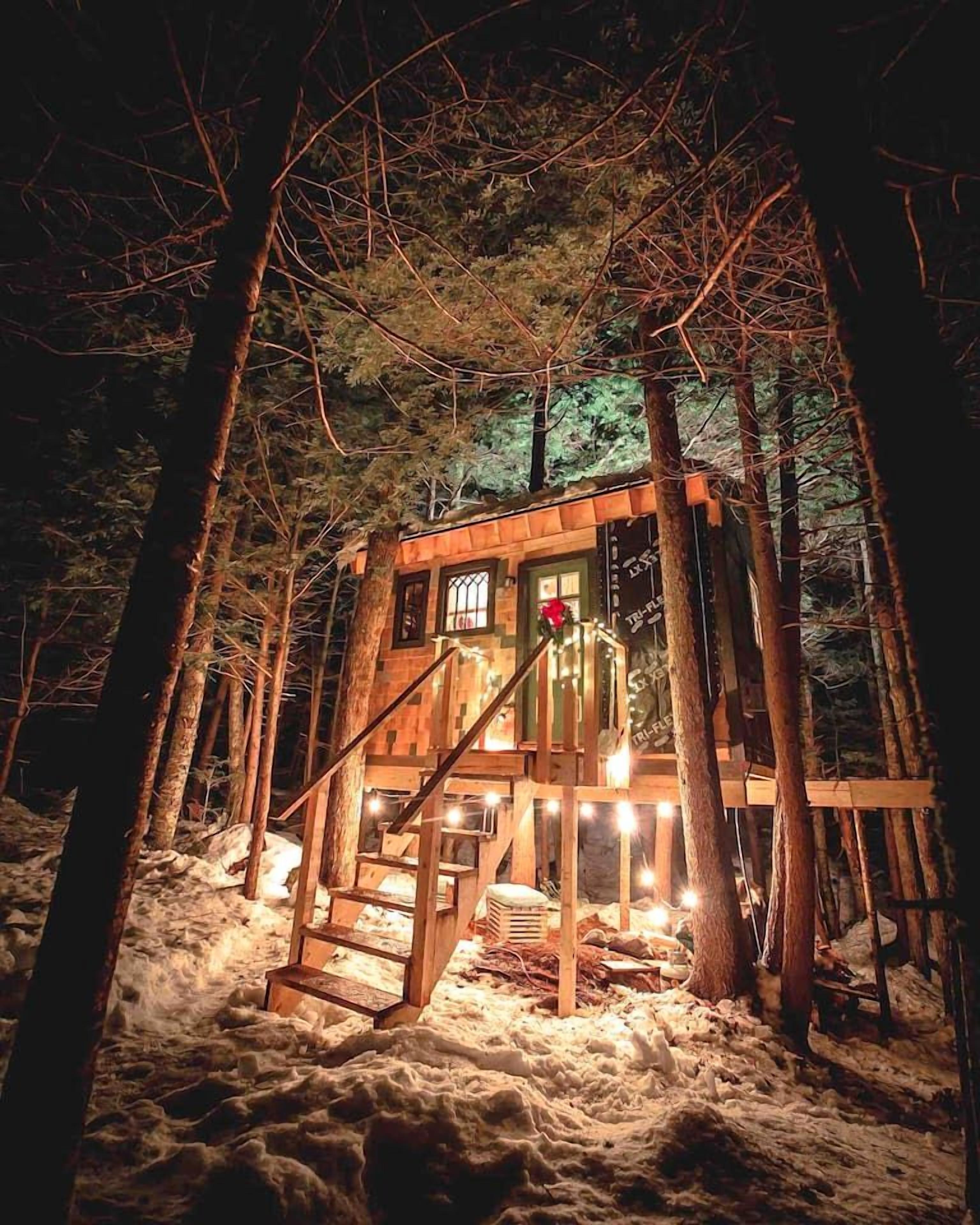 A wooden cabin with a staircase, surrounded by trees and snow.