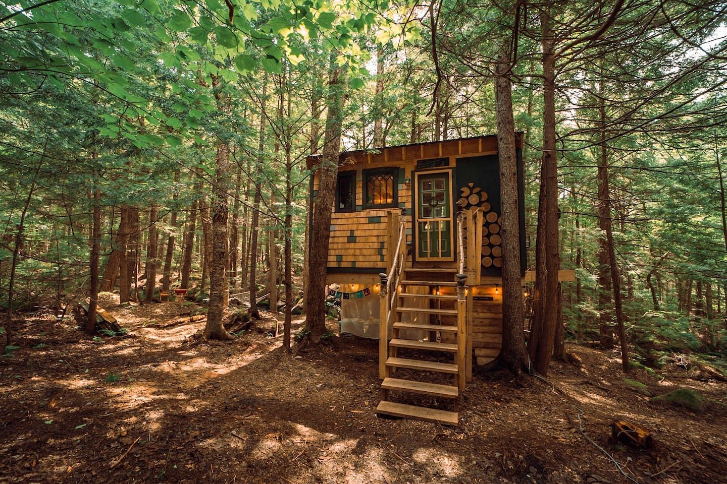 A wooden cabin with a staircase leading to a door, surrounded by a forest.