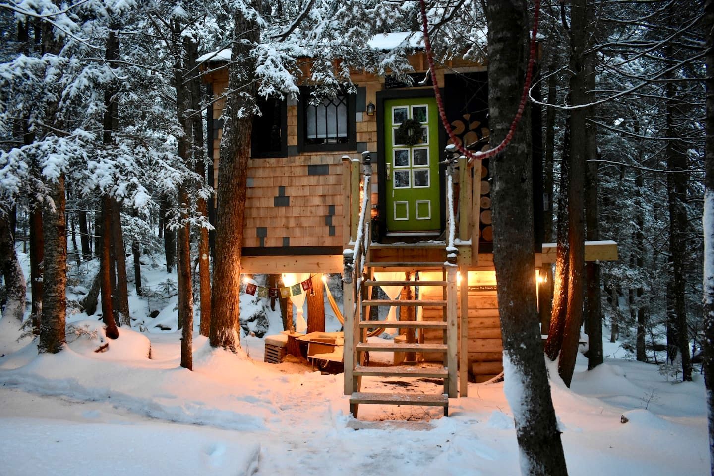 En stuga av trä med en grön dörr, omgiven av snötäckta träd.