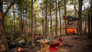 A forest cabin with a dining area featuring a table and chairs, a fire pit, and a wooden deck.
