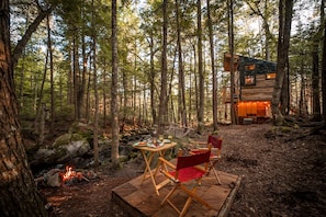 A forest cabin with a dining area featuring a table and chairs, a fire pit, and a wooden deck.