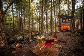 A forest cabin with a dining area featuring a table and chairs, a fire pit, and a wooden deck.