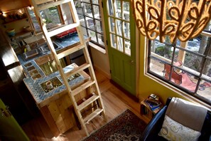 A room with a wooden ladder, a tiled backsplash, a green door, and a view through a window. - Cozy Treehouse with Sauna in Hardwick, VT (Hardwick)