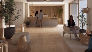 Zona de recepción moderna de un hotel, con un mostrador de madera, plantas en macetas y un área de descanso con un amplio ventanal.