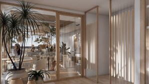 Un interior moderno con suelo de madera, plantas grandes en macetas y un separador de vidrio que divide el comedor del área de trabajo.