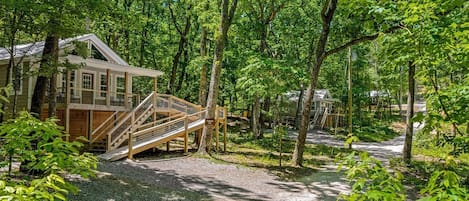 Eine Holzhütte mit einer Holztreppe, die zu einer Terrasse führt, umgeben von dichtem Wald.