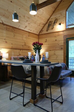 Ein Holzinterieur mit Esstisch, Stühlen, einer Vase mit Blumen und einer Bank.