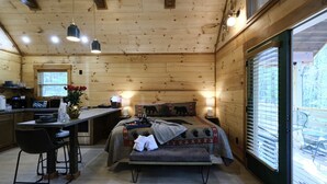 Una baita con cucina, zona pranzo e camera da letto con un letto, una panca e una finestra.