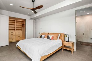 Ein Schlafzimmer mit Bett, Holzschrank, Deckenventilator, Nachttisch und Beistelltisch.