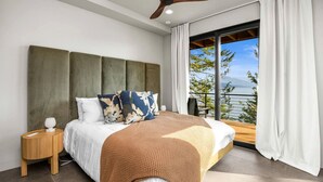 A bedroom with a bed, a nightstand, a ceiling fan, and a large window with curtains.