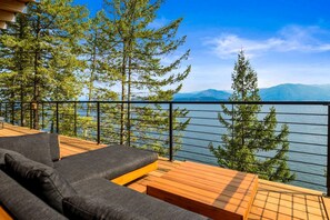 Una terraza con sofá y mesa de madera, con vistas a un lago y montañas.
