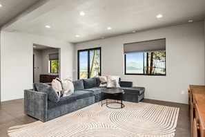A modern living room with a sectional sofa, a coffee table, and a view of the outdoors through large windows.