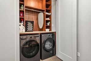 A laundry room with two front-loading washing machines, a drying rack, and storage shelves.