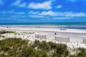 A beach with a wooden fence, sand dunes, and a clear blue sky.