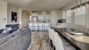 Cozinha moderna com armários brancos, uma ilha central com banquetas e uma área de jantar com mesa grande e cadeiras.