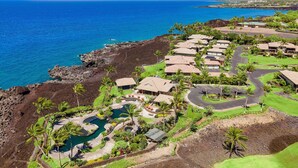 An aerial view of a resort with multiple bungalow-style buildings, a central pool area, and a view of the ocean. - Complete Remodel Stunning Ocean Views Discount of Golf (Waikoloa)