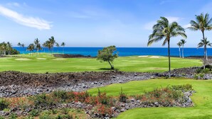 A golf course with a view of the ocean, palm trees, and a clear sky. - Complete Remodel Stunning Ocean Views Discount of Golf (Waikoloa)