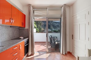 A kitchen with orange cabinets, a granite countertop, and a sliding glass door leading to a balcony with outdoor furniture. - Vacation Studio 'Estrella' with Mountain View, Wi-Fi and Air Conditioning (Puerto de Mogán)