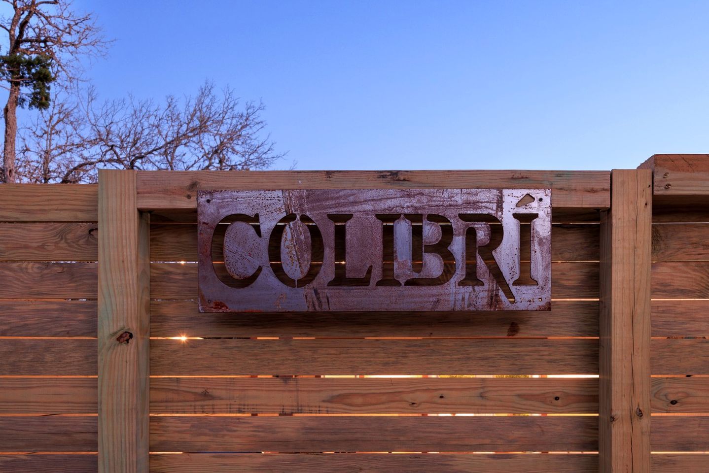 Een houten hek met een metalen bord waarop 'COLIBRI' staat.