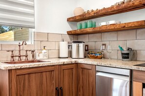 A kitchen with a granite countertop, wooden cabinets, a stainless steel dishwasher, and a built-in oven. - Impressive Intimate Tiny Cabin with Lofted Interior and Outdoor Shower in Texas (Wimberley)