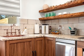 A kitchen with a granite countertop, wooden cabinets, a stainless steel dishwasher, and a built-in oven. - Impressive Intimate Tiny Cabin with Lofted Interior and Outdoor Shower in Texas (Wimberley)