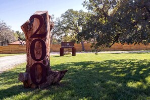 A large wooden number '200' sign, a wooden fence, and a sign for 'AVANDARO RANCH' in a grassy area with trees. - Impressive Intimate Tiny Cabin with Lofted Interior and Outdoor Shower in Texas (Wimberley)