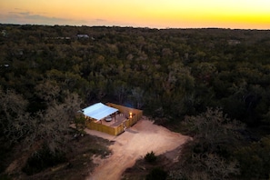 A remote cabin with a metal roof, surrounded by dense forest, accessible by a dirt path. - Impressive Intimate Tiny Cabin with Lofted Interior and Outdoor Shower in Texas (Wimberley)