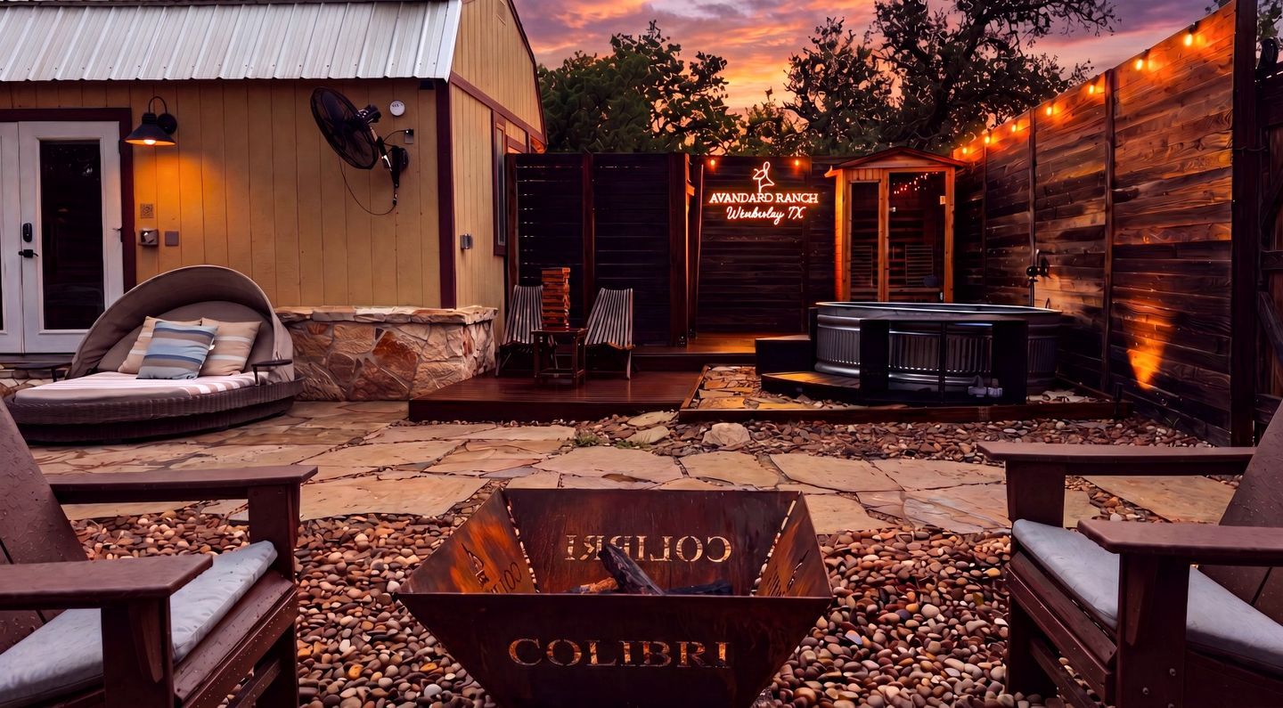 A rustic outdoor seating area with a fire pit, lounge chairs, and a wooden fence.